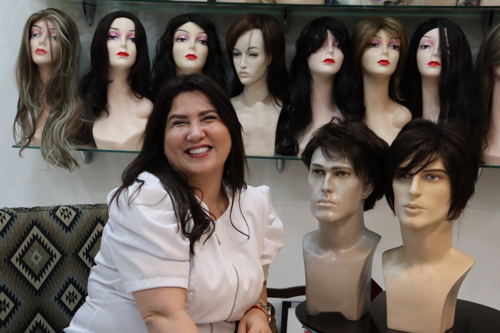Cristina Orosa sorrindo entre a vitrine de perucas premium do seu ateliê em Santos